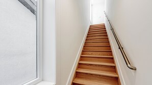 Una escala de fusta amb barana, parets blanques i una finestra a la part superior.