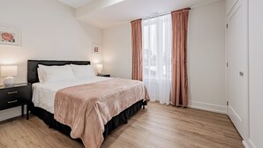 Un dormitori amb un llit, taules de nit, una finestra amb cortines i una porta.