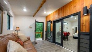A modern living room with a leather sofa, a lamp, and a view of a dining area through glass doors. - Double Magic - Unique cabin for 6 - pond, hot tub (Broken Bow)