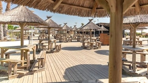 Eine Holzterrasse mit reetgedeckten Sonnenschirmen und Holztischen, die an eine Lage am Strand erinnert.