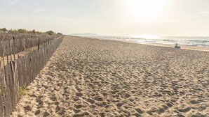 Ein Strand mit einer Holzlattenveranda, einer Person auf einem Promenadendeck und dem Meer im Hintergrund.