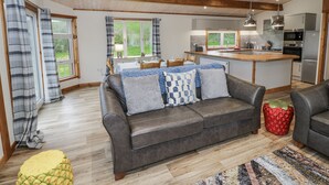 A modern kitchen with a central island, wooden beams on the ceiling, and a dining area with a table and chairs. - Willow Lodge (Rugeley)
