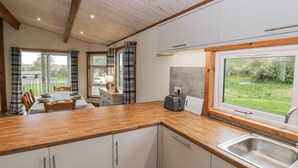 A modern kitchen with wooden cabinets, a stainless steel sink, and a view of the garden. - Willow Lodge (Rugeley)