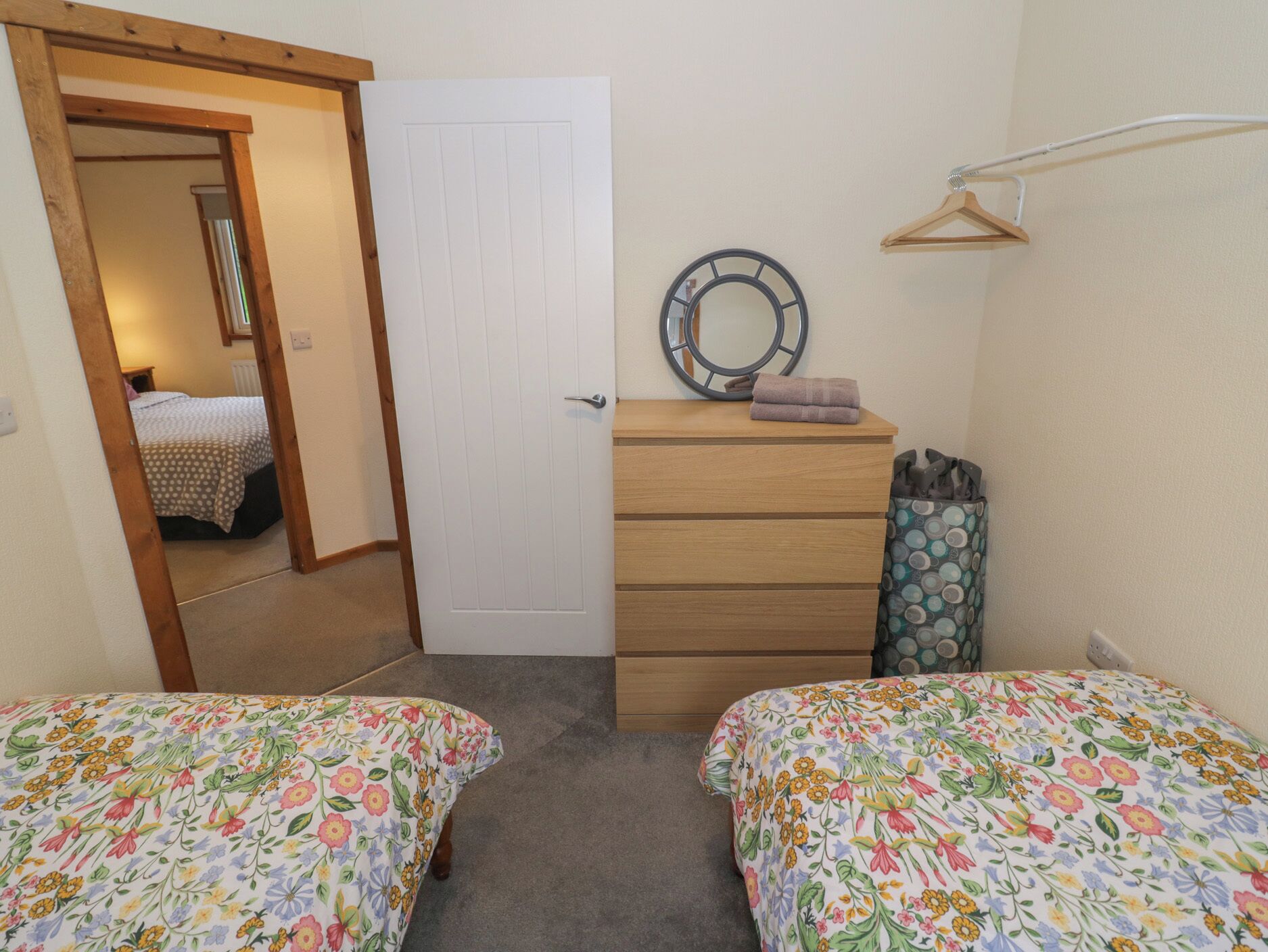 A bedroom with two beds, a wooden dresser, a mirror, and a hanging towel rack.