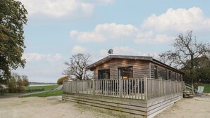 En træhytte med hegnede terrasse, en lille veranda og udsigt over det omkringliggende landskab.