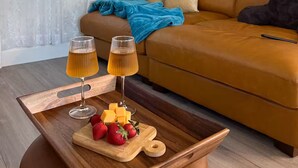 A living room with a brown sofa, a wooden coffee table with a glass of wine and fruit, and a painting on the wall. - Earthy Luxe Guesthouse-Fully Fenced- W/D in unit (Hesperia)