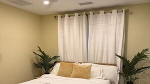A neatly made bed with a blue blanket and white linens, a ceiling fan, and a nightstand with a plant. - Earthy Luxe Guesthouse-Fully Fenced- W/D in unit (Hesperia)