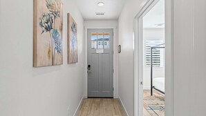 Un couloir étroit avec une porte grise, un plancher en bois et deux tableaux représentant des motifs floraux accrochés au mur.