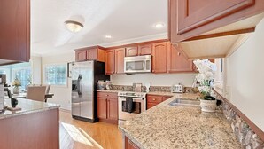 A spacious kitchen with granite countertops, wooden cabinets, stainless steel appliances, and a stone backsplash.