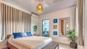 A modern bedroom with a large bed, a hanging light fixture, and a view of a bathroom. - Ela Kosher Hotel and Jewish Center (Jaco)