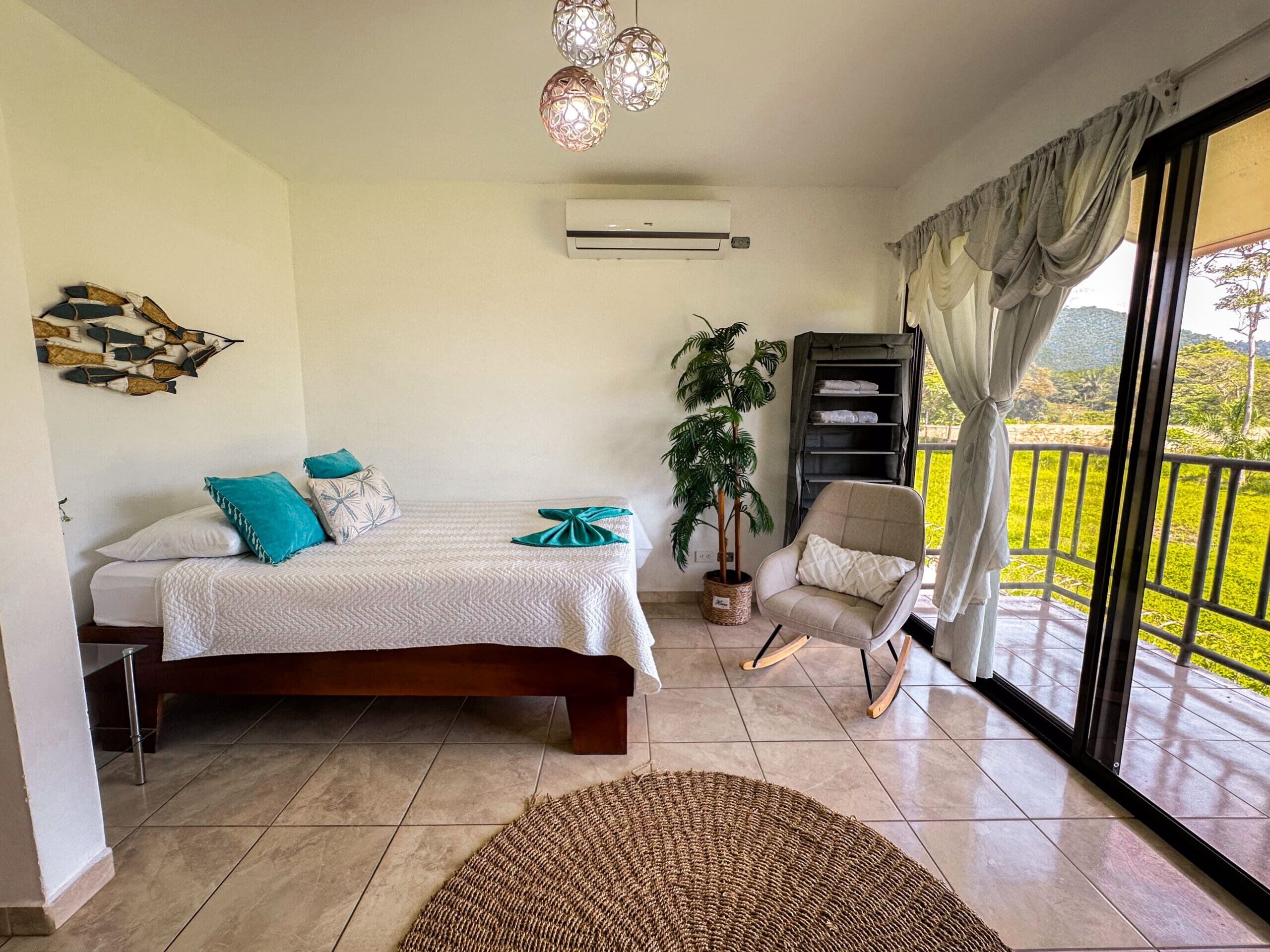 Un dormitorio con cama, una silla, una planta en maceta y vistas al exterior.