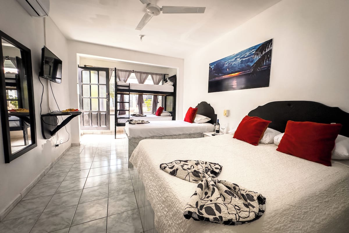 A hotel room with two beds, a TV, a ceiling fan, and a painting of a cityscape.