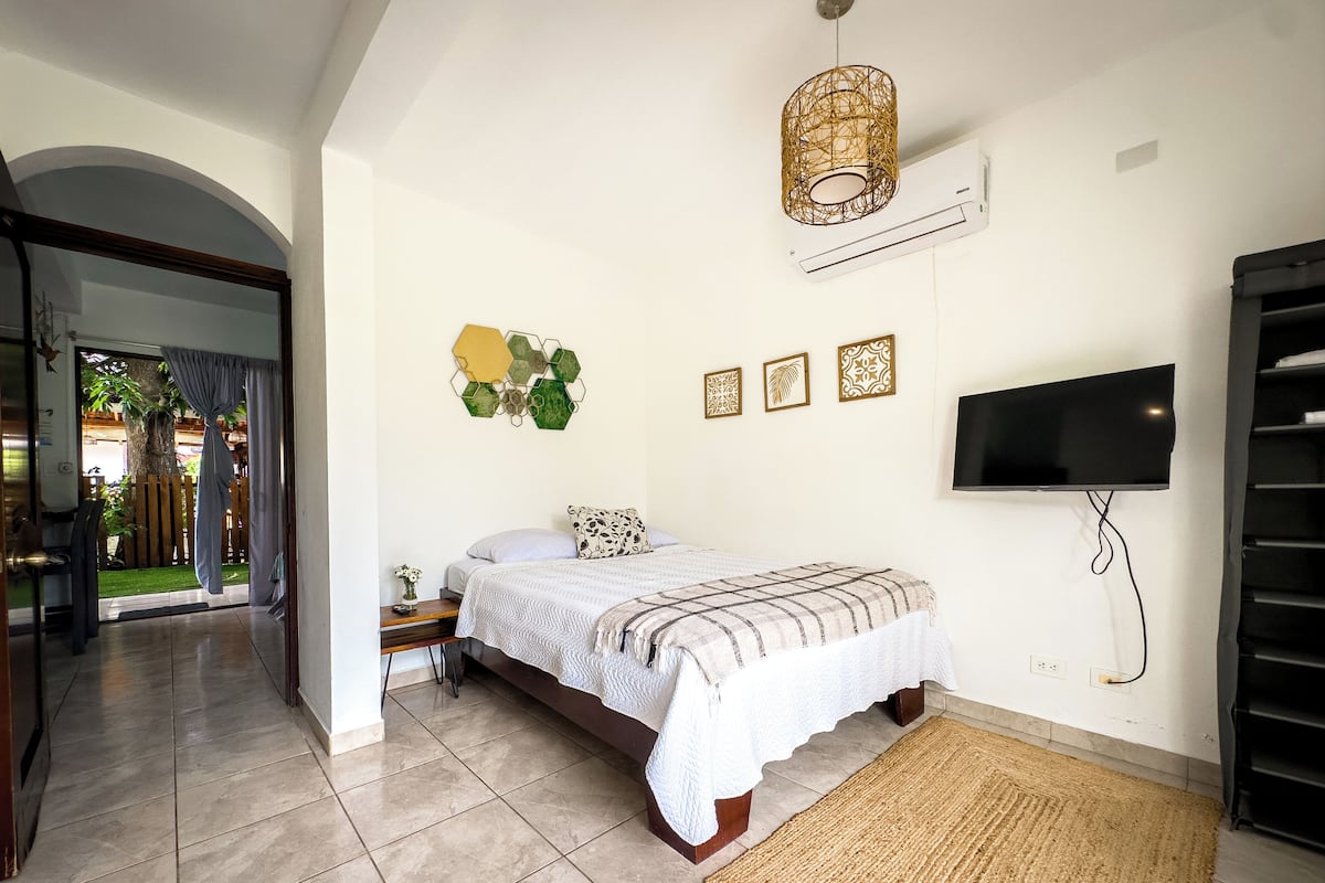 A bedroom with a bed, a TV, a wall-mounted air conditioner, and a door leading to a balcony.