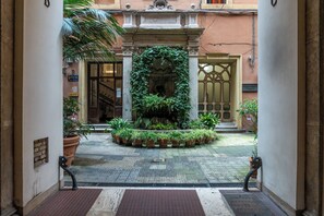 A courtyard with a central fountain, surrounded by potted plants and a wrought iron gate. - Ricci Rooms Nazionale (Rome)