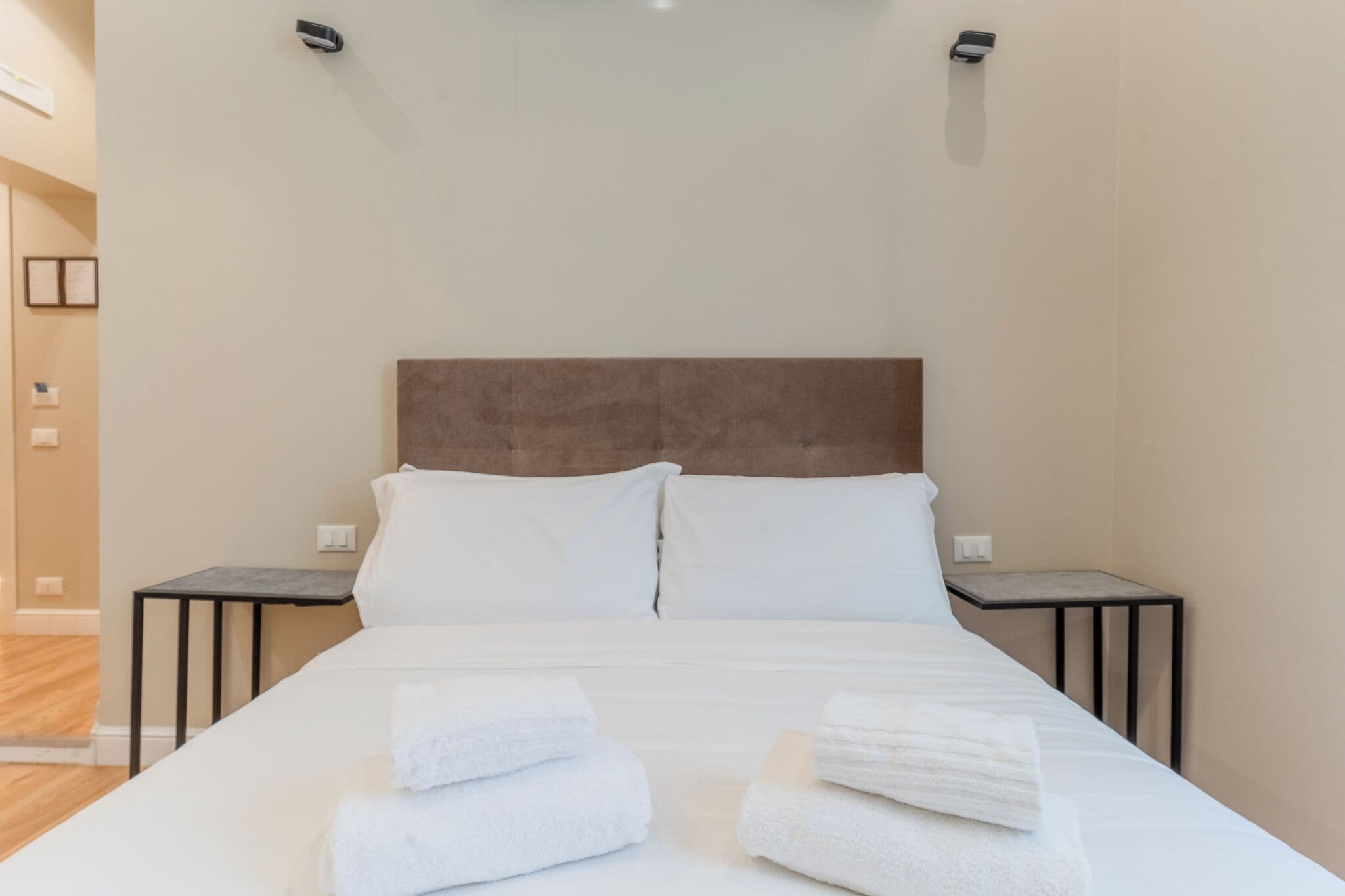 A neatly made bed with white linens and towels, a wooden headboard, and two bedside tables.