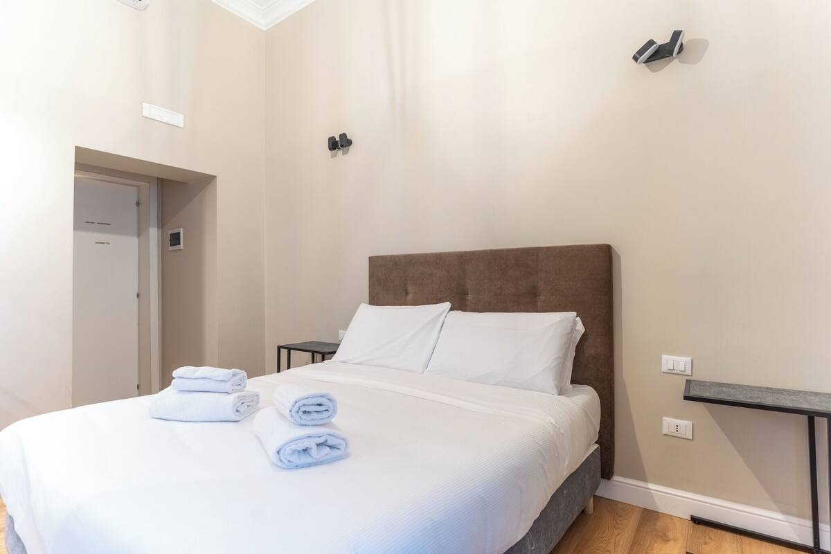 A neatly made bed with white linens and towels, a brown headboard, and a small bedside table with a lamp.
