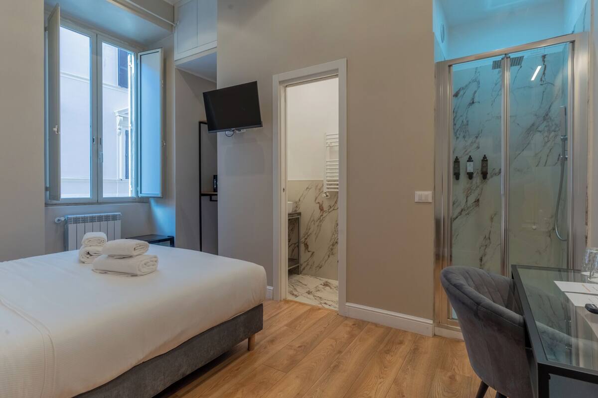 A bedroom with a bed, a TV, a shower, and a glass table.