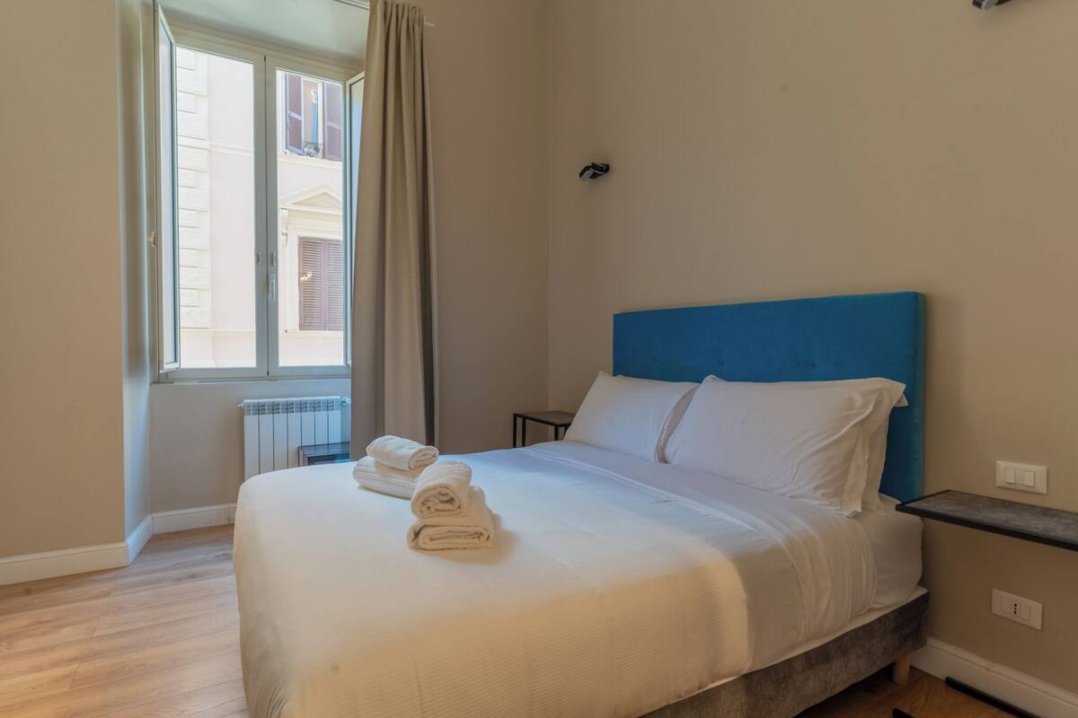 A hotel room with a bed, a window, a radiator, and a nightstand.