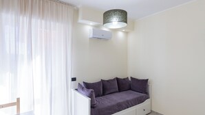 Une chambre moderne avec un canapé-lit blanc, une petite table et un luminaire au plafond.