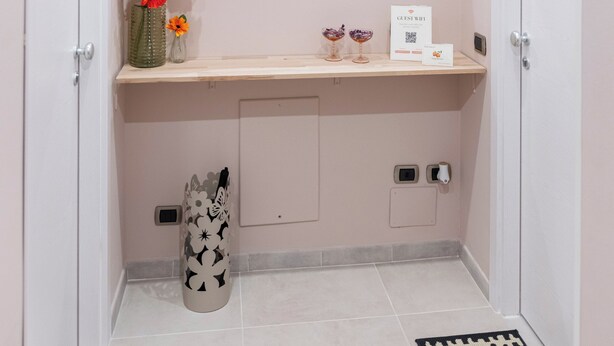 Une salle de bain avec un meuble-lavabo, un miroir, une balance, un vase à fleurs et une porte dotée d’une poignée.