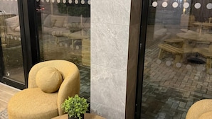 A modern lounge area with a round wooden table, a beige armchair, and a small potted plant.
