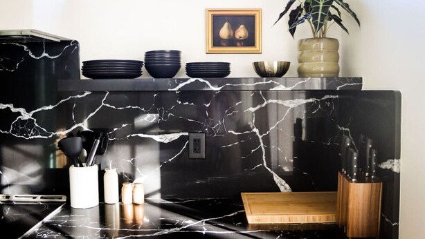 A kitchen with a black marble countertop, a wooden cutting board, and a knife block.