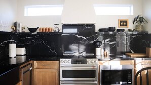 A modern kitchen with black marble countertops, stainless steel appliances, and wooden cabinets.