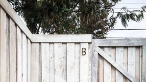A white wooden gate with a 'B' marking, a concrete pathway, and a small garden area with plants.