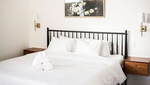 A neatly made bed with white linens and rolled towels, a black metal headboard, and a framed picture on the wall.