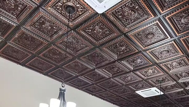 A dining area with a high, intricately designed ceiling, a chandelier, and a modern kitchen with a refrigerator.