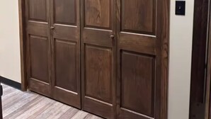 A wooden sliding door with a panel design, leading to a room with a wooden floor.