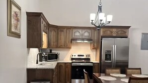 A kitchen with wooden cabinets, a stainless steel refrigerator, a microwave, and a dining table with chairs.