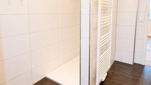 Un baño moderno con azulejos blancos, un radiador blanco y un suelo marrón oscuro.