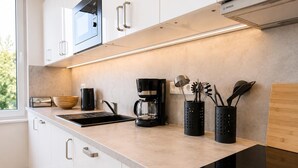 Una cocina moderna con armarios blancos, una cafetera negra y utensilios en organizadores.