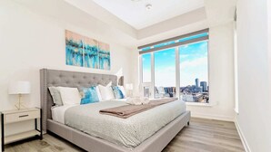 Un dormitorio moderno con una cama grande, vistas a la ciudad y un cuadro en la pared.