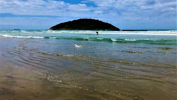 A beach with waves, a distant island, and a ship in the water. - Apartamento Vista Mar em Imbituba (Imbituba)
