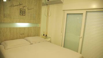 Un dormitorio con una cama, una mesita de noche con espejo y una ventana con persianas.