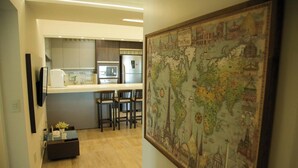 A modern kitchen with stainless steel appliances and a dining area with two chairs. A large world map is displayed on the wall. - Apartamento Vista Mar em Imbituba (Imbituba)
