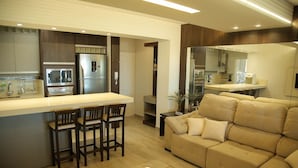 A modern kitchen with a central island, bar stools, and a beige sofa in a living area. - Apartamento Vista Mar em Imbituba (Imbituba)
