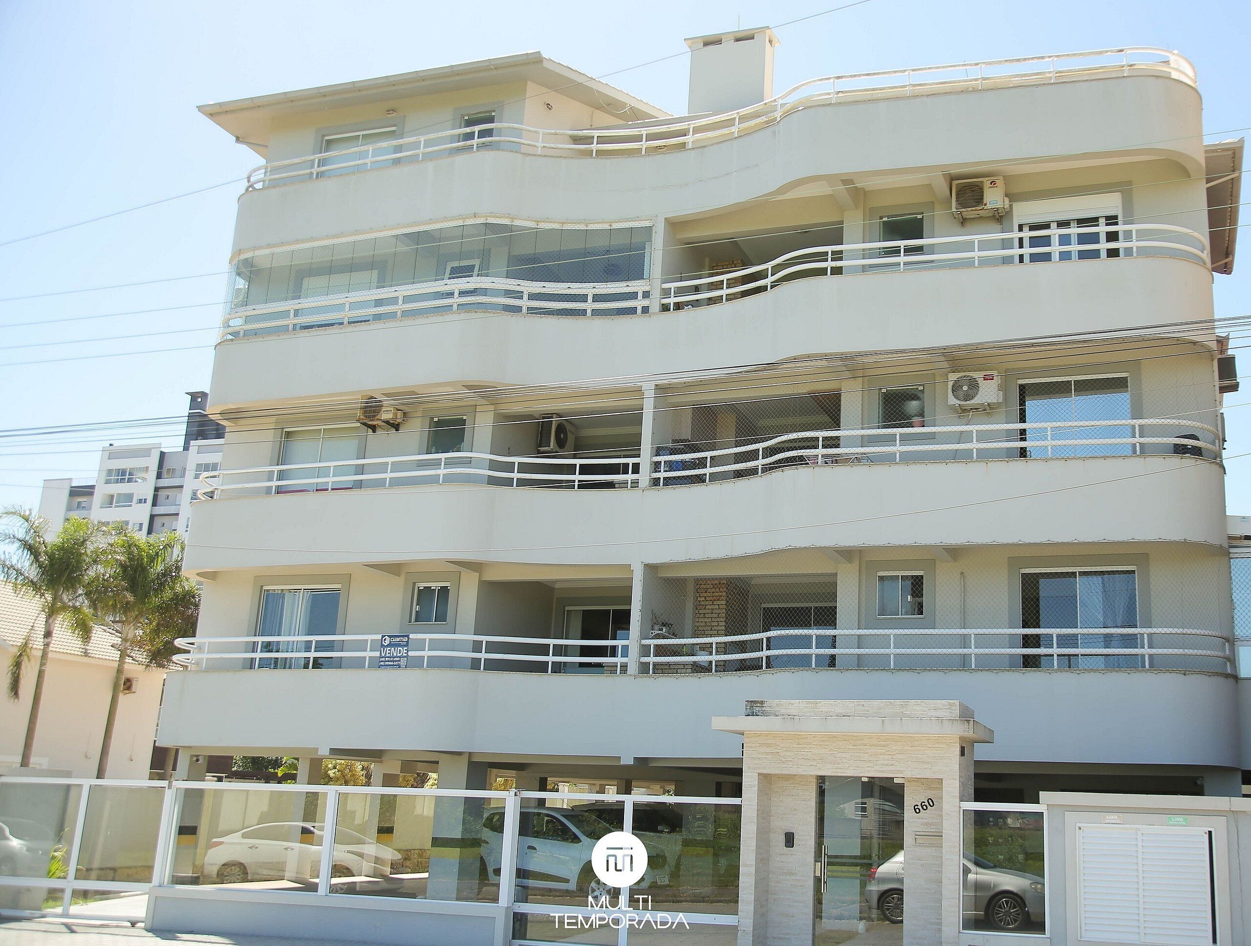 Un edificio de varios pisos con balcones, un coche estacionado adelante y un letrero que anuncia una venta.