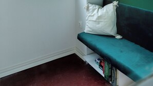 Une pièce d’angle avec une fenêtre, un mur vert, un banc blanc et un coussin blanc.