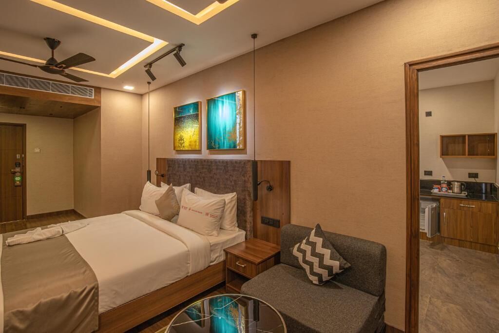 A hotel room with a bed, a sofa, a small table, and a ceiling fan.