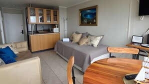 A compact living space with a kitchenette, a sofa, a dining table, and a painting on the wall. - Oceana Suites EuroMarina II (Viña del Mar)