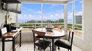 A dining area with a table and chairs, a television, and a view of buildings and the sea. - Oceana Suites EuroMarina II (Viña del Mar)