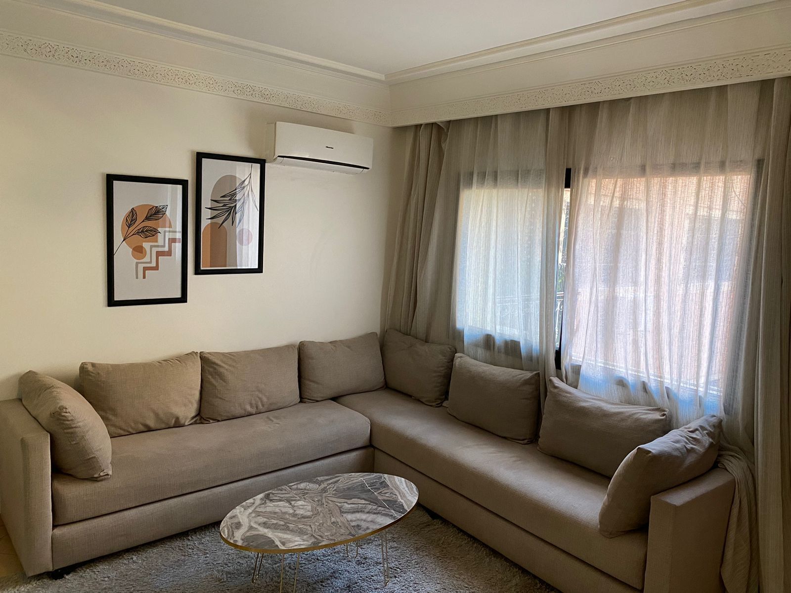Una sala de estar con un sofá color beige, una mesa de centro de mármol y dos cuadros enmarcados en la pared.