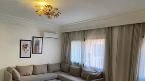 Un salon avec un canapé d’angle beige, une table basse ronde et un lustre.