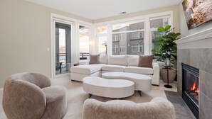 A modern living room with a sectional sofa, round ottomans, and a fireplace. - Puget Sound Views Elegant 2BR Walk to Pike Place (Seattle)