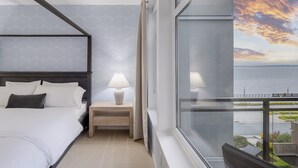 A hotel room with a bed, bedside table, lamp, and a large window offering a view of the sea. - Puget Sound Views Elegant 2BR Walk to Pike Place (Seattle)