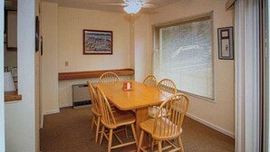 Uma área de refeições com uma mesa e cadeiras de madeira, um quadro na parede e uma janela com persianas.
