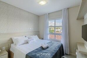 A hotel room with a neatly made bed, a window with curtains, a flat-screen TV, and a wooden headboard. - Apt w/ BBQ & View, 130m From Beach Rsd0202 (Porto Belo)